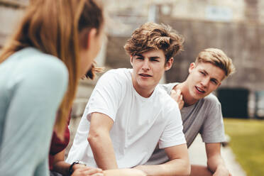 Group of friends sitting at school campus and talking. Teenage boys and girls sitting at high school campus during break. - JLPSF24352