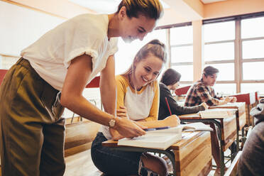 Glückliche Lehrerin, die einem Teenager im Klassenzimmer hilft. Professorin, die einer Schülerin während eines Unterrichts in der High School hilft. - JLPSF24354