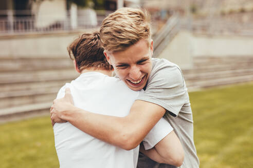 Zwei Jungen umarmen sich auf dem College-Campus. High-School-Schüler lächeln und umarmen sich im Freien. - JLPSF24386