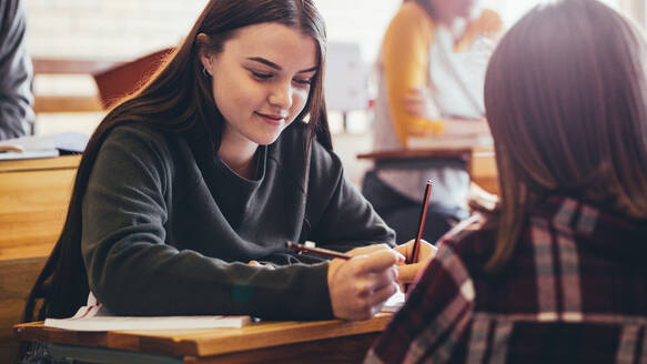 Mädchen sitzen am Schreibtisch im Klassenzimmer. Studentinnen lernen zusammen in der High School. - JLPSF24388
