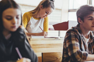 Teenager-Mädchen sitzt an ihrem Schreibtisch im Klassenzimmer der High School und schreibt in ein Notizbuch. Studentin macht Notizen während einer Vorlesung in der Schule. - JLPSF24391