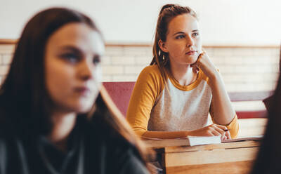 Schönes Mädchen sitzt in der Klasse mit Klassenkameraden um die Aufmerksamkeit auf den Vortrag zu zahlen. Junge Menschen studieren an der High School. - JLPSF24392