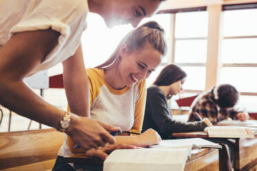 Junge Frau studiert mit einem Lehrer, der im Klassenzimmer steht. High-School-Lehrer hilft Schülern im Klassenzimmer. - JLPSF24398