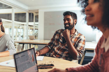 Coworkers in a meeting discussing business plans and ideas. Businessman sitting with female colleagues in conference room in office. - JLPSF24399