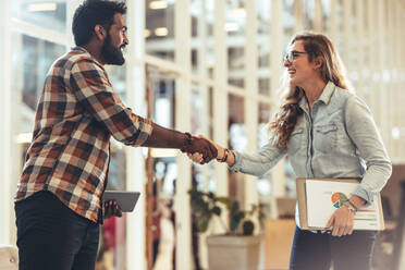 Business partners shaking hands after a discussion. Woman entrepreneur holding official papers greeting a business client at work place. - JLPSF24403