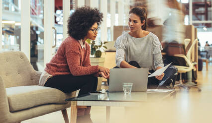 Geschäftsfrauen tauschen Ideen aus, während sie mit einem Laptop auf dem Tisch sitzen. Unternehmerinnen in einer Besprechung in einer Lounge am Arbeitsplatz. - JLPSF24404