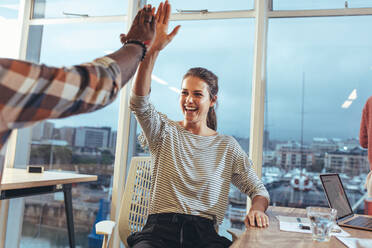 Business colleagues giving high five to each other in office. Team members celebrating success at work by giving high five. - JLPSF24422