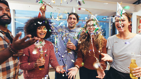 Happy businessmen and women holding drinks having fun at a party. Friends having a get together party enjoying drinks with confetti flying around. - JLPSF24428