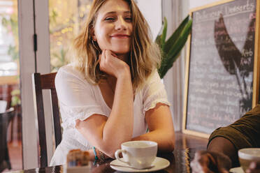 Happy young woman sitting at cafe with her friend. Relaxed female sitting at coffee shop with a male friend. - JLPSF24429