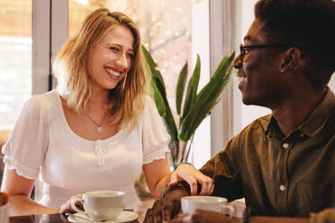 Junge Frau trifft ihre Freundin in einem Café. Glückliches gemischtrassiges Paar sitzt zusammen im Café. - JLPSF24430