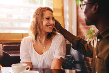 Ein gemischtrassiges Paar sitzt in einem Café. Lächelnde Frau mit ihrem fürsorglichen Freund im Café. - JLPSF24431