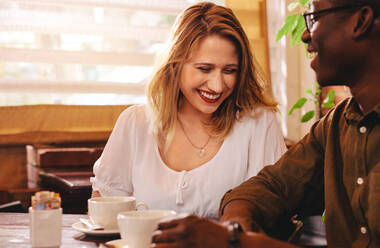 Fröhliche Frau sitzt mit ihrem Freund am Cafétisch. Multi-ethnisches Paar im Café. - JLPSF24432