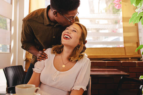 Afrikanischer Mann mit seiner Freundin, die sich in einem Café auf die Stirn küsst. Glückliches Paar bei einem Date in einem Café. - JLPSF24437