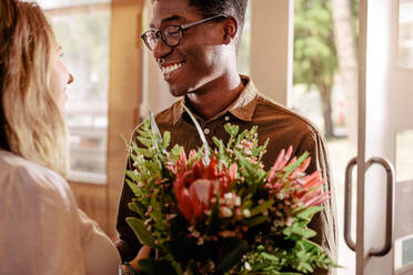 Junger afrikanischer Mann mit Blumenstrauß beim Treffen mit seiner Freundin. Mann gibt Blumen an das geliebte Mädchen beim Date. - JLPSF24440