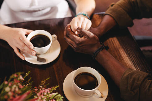 Nahaufnahme eines Mannes, der die Hand einer Frau auf einem Tisch mit Kaffeetassen an der Seite hält. - JLPSF24442