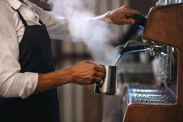 Mitarbeiter eines Coffeeshops bereitet Kaffee auf einer Dampf-Espressomaschine zu. Ausschnitt eines Mannes, der in einem Coffeeshop arbeitet und eine Schürze trägt. - JLPSF24458