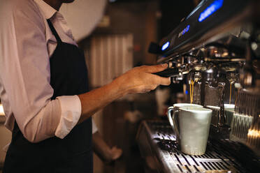 Ausschnitt eines Barista, der eine Kaffeemaschine benutzt, um eine Tasse Kaffee zuzubereiten. Eine weibliche Caféangestellte macht einen Kaffee. - JLPSF24459