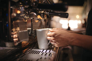 Nahaufnahme eines Barista, der eine Tasse unter der Kaffeemaschine hält. Eine weibliche Caféangestellte bereitet Kaffee in der Maschine zu. - JLPSF24460