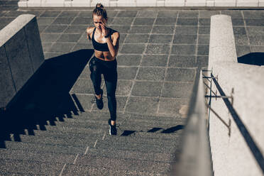 Eine fitte Sportlerin läuft die Treppe hinauf. Eine Läuferin trainiert auf einer Treppe im Freien. - JLPSF24474