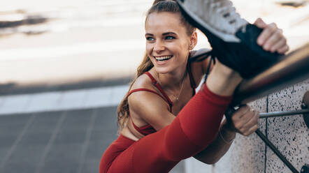 Eine fitte Sportlerin macht Dehnübungen auf einem Geländer. Eine Sportlerin macht Aufwärmübungen im Freien. - JLPSF24481