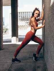 Sportlerin in voller Länge bei Dehnungsübungen an einer Wand im Freien. Fitness-Frau beim Training an einer Wand. - JLPSF24486