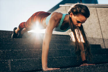 Starke junge Frau macht Liegestütze auf Stufen im Freien. Sportlerin macht Liegestütze Übungen am Morgen. - JLPSF24494