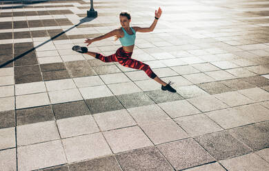 Fitness-Frau macht Spagatsprung im Freien in der Stadt. Flexible weibliche Athletin trainiert im Freien. - JLPSF24499