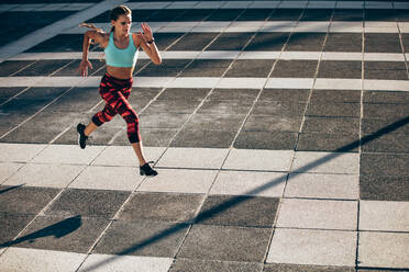 Sportliche Frau beim Laufen und Springen im Freien in der Stadt. Weibliche Athletin in Laufkleidung beim Training am Morgen. - JLPSF24501
