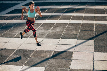 Sports woman in running and jumping outdoors in the city. Female athlete in running attire exercising in morning. - JLPSF24501