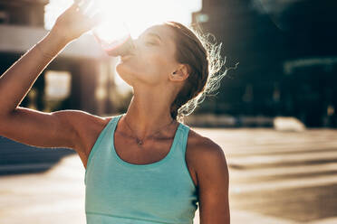 Fit young woman drinking water after workout session. Thirsty female athlete drinking water outdoors. - JLPSF24502