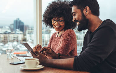 Geschäftsmann und Frau sitzen im Büro und besprechen die Arbeit mit einem Tablet-Computer. Glückliche Business-Kollegen sitzen am Schreibtisch und arbeiten. - JLPSF24516