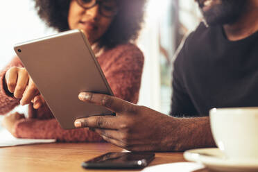 Close up of a businessman and businesswoman sitting together at work looking at a tablet computer. Man holding a tablet computer while a businesswoman is pointing at the screen. - JLPSF24517