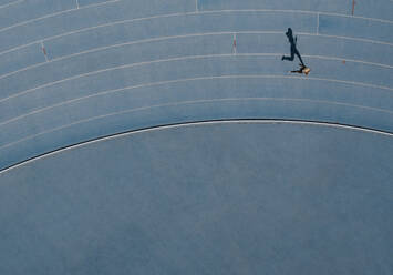 Sprinter running on athletic track. Top view of a sprinter running on race track in a stadium with shadow falling on the side. - JLPSF24526