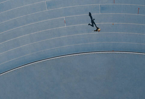 Luftaufnahme einer Athletin, die auf einer Leichtathletikbahn läuft. Draufsicht auf eine Sprinterin, die auf einer Rennbahn in einem Stadion läuft. - JLPSF24527