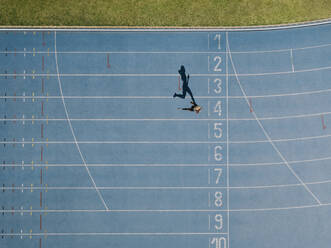 Female sprinter running on athletic track nearing the finish line. Top view of a sprinter running on race track in a stadium. - JLPSF24529