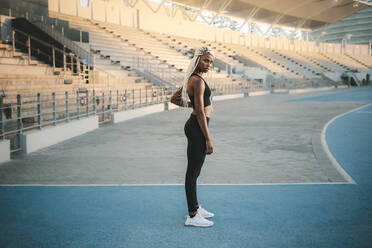 Female athlete standing inside a track and field stadium ready. Female runner getting ready to warm up and workout before running. - JLPSF24531