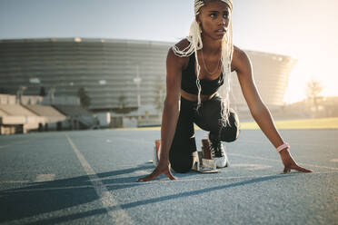 Athletin, die sich auf die Markierungen stellt, um den Lauf zu beginnen. Eine Läuferin übt ihren Sprint auf einer Allwetterlaufbahn in einem Stadion. - JLPSF24543