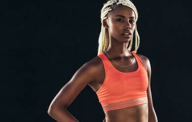 Porträt einer Sportlerin auf schwarzem Hintergrund. Sprinterin in Fitnesskleidung, stehend mit Hand an der Hüfte. - JLPSF24559