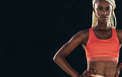 Porträt einer Sportlerin auf schwarzem Hintergrund. Sprinterin in Fitnesskleidung, stehend mit den Händen auf der Hüfte. - JLPSF24561