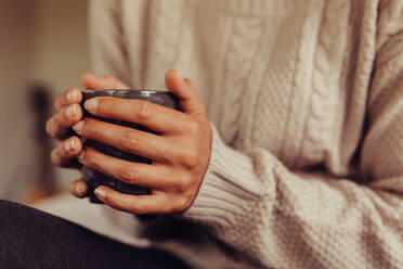 Close up of female with a cup of tea. Cropped shot of woman having morning tea in bed. Focus on hands holding a tea cup. - JLPSF24591