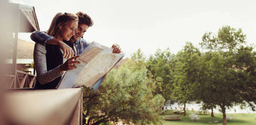 Ein Ehepaar steht vor seinem Ferienhaus und sucht auf einer Karte nach dem Weg. Ein Mann und eine Frau im Urlaub suchen auf einer Karte nach dem Ort. - JLPSF24599