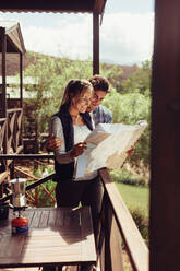 Couple standing in their hotel room balcony and looking at map. Man and woman reading map for finding nearest tourist attraction. - JLPSF24601