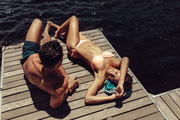 Junges Paar, das sich auf einem Steg am See entspannt. Frau im Bikini liegt mit ihrem Freund auf einem Holzsteg am See. - JLPSF24616