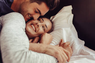 Lächelndes junges Paar liegt zusammen auf dem Bett. Romantisches junges Paar liegt im Bett. - JLPSF24621