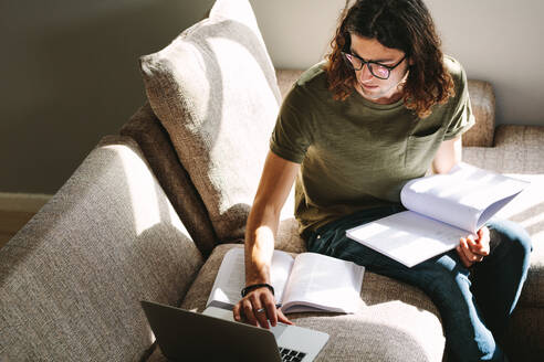 Männlicher Student, der sich zu Hause sitzend auf College-Prüfungen vorbereitet und dabei auf einen Laptop blickt. - JLPSF24626