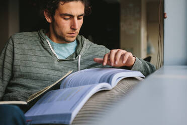 Schüler, der auf einer Couch sitzend ein Buch liest und Notizen schreibt. Schüler, der zu Hause sitzt und aus einem Lehrbuch lernt. - JLPSF24648
