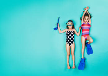 Zwei liegende Mädchen mit Schnorchel und Schwimmflossen. Draufsicht auf Zwillingsmädchen in Badekleidung auf blauem Hintergrund. - JLPSF24701