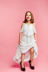 Girl wanting to be a grown up woman, wearing oversized dress and shoes over pink background. Girl in her mother's outfit looking at camera and smiling. - JLPSF24738