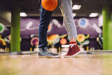 Ausschnitt eines Liebespaares, das auf einer Bowlingbahn eng beieinander steht. Fokus auf die Beine von Mann und Frau mit der Bowlingkugel. - JLPSF24748