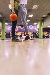 Ausschnitt eines Paares, das mit einer Kugel in einem Bowling-Club zusammensteht. Beine eines Mannes und einer Frau mit einer Kugel auf einer Bowlingbahn. - JLPSF24749